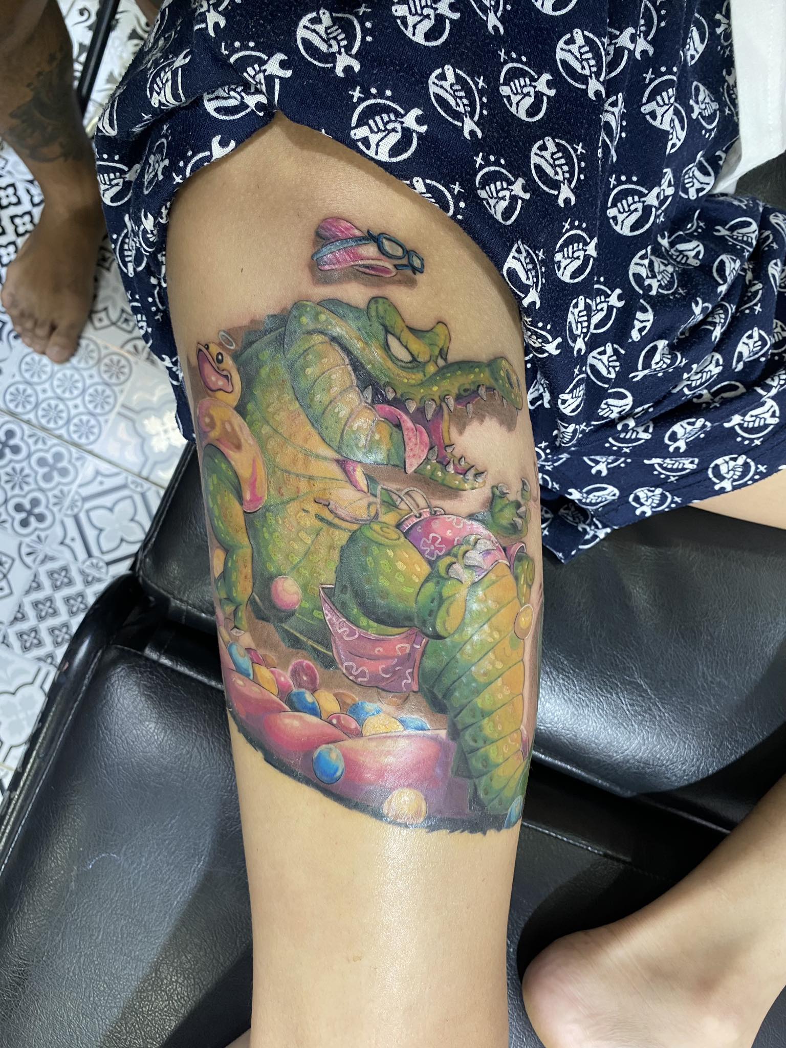Alligator, Jewels, Color, Thigh, Character Tattoo by Max. He is a highly skilled tattoo artist at Lethal Ink Tattoo in Pattaya. He is celebrated for is expertise in black and grey, anime, manga, Thai art, and tribal motifs. Max, Alligator, Jewels, Color, Thigh, Character Tattoo, Lethal Ink, Pattaya, 2024