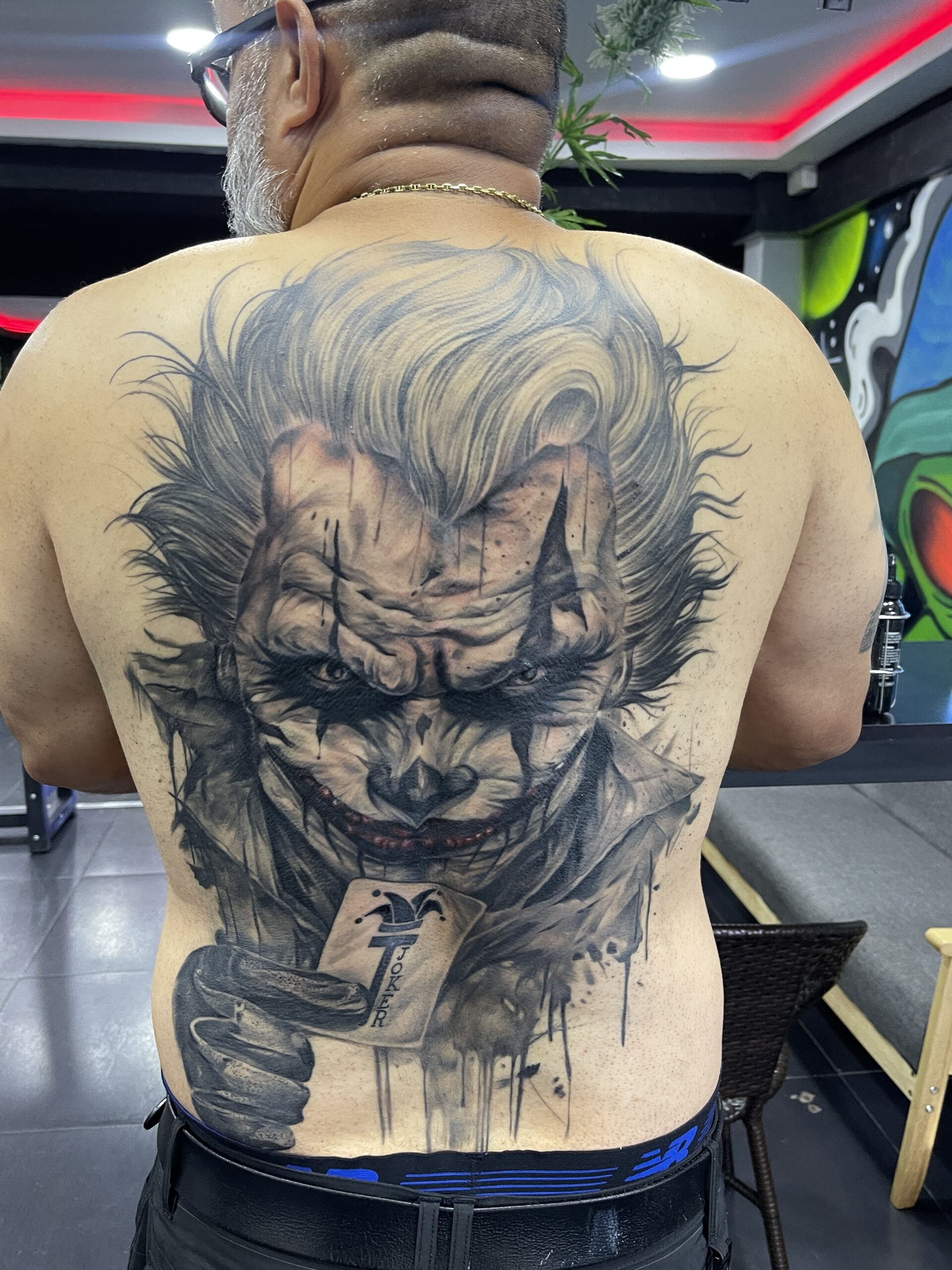 Black and grey, Joker, Back Tattoo by Max. He is a highly skilled tattoo artist at Lethal Ink Tattoo in Pattaya. He is celebrated for his expertise in black and grey, anime, manga, Thai art, and tribal motifs. Max, black and grey, Joker, Back Tattoo, Lethal Ink, Pattaya, 2024