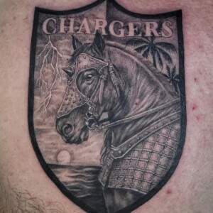 Black realistic charger crest tattoo on chest by Sandy at Lethal Ink Tattoo, Pattaya. Sandy specializes in Realism, Black & Grey, Illustrative, Portrait, and Neo Traditional styles. Black realistic charger crest tattoo on chest by Sandy, tattoo artist at Lethal Ink Tattoo, Pattaya (2025)