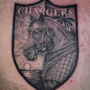 Black realistic charger crest tattoo on chest by Sandy at Lethal Ink Tattoo, Pattaya. Sandy specializes in Realism, Black & Grey, Illustrative, Portrait, and Neo Traditional styles. Black realistic charger crest tattoo on chest by Sandy, tattoo artist at Lethal Ink Tattoo, Pattaya (2025)
