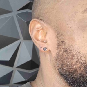 Piercing de un solo anillo en el lóbulo de la oreja izquierda con un pendiente de acero quirúrgico negro en Lethal Ink Tattoo Pattaya. Perforación de lóbulo de oreja con un solo anillo y un pendiente de acero quirúrgico negro en la oreja izquierda en Lethal Ink Tattoo Pattaya (2026)