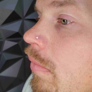 Piercing nasal con pendiente de gema transparente en el lado izquierdo en Lethal Ink Tattoo Pattaya. Piercing de aro único en la fosa nasal con gema transparente y pendiente de acero quirúrgico en el lado izquierdo en Lethal Ink Tattoo Pattaya (2026)
